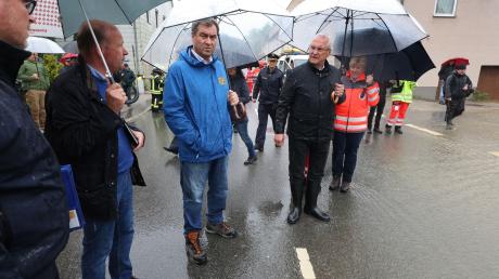 Markus Söder (CSU, l), bayerischer Ministerpräsident und Joachim Herrmann, bayerischer Innenminister (CSU, M), stehen am Rande einer überfluteten Straße.
