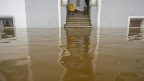 Im Treppenaufgang eines Hauses, dessen Untergeschoss voll Wasser ist, stehen Gummistiefel.