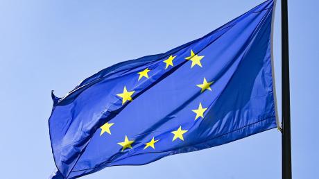 Eine Europaflagge weht vor blauem Himmel. Die Flagge der EU ist blau mit goldenen Sternen darauf.