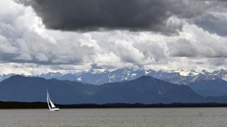 Ein Segelboot ist auf dem Starnberger See unterwegs während Gewitterwolken über die Alpen ziehen.