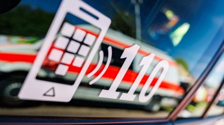 Die Nummer des Polizeinotrufs 110 steht auf der Scheibe eines Polizeifahrzeugs, in der sich ein Fahrzeug vom Roten Kreuz spiegelt.