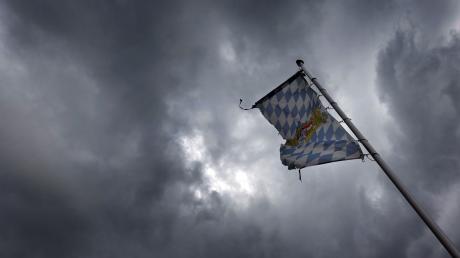 Eine Bayernfahne weht vor dichten Regenwolken im Wind.