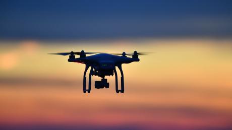 Eine Drohne  fliegt bei Sonnenuntergang über eine Wiese.