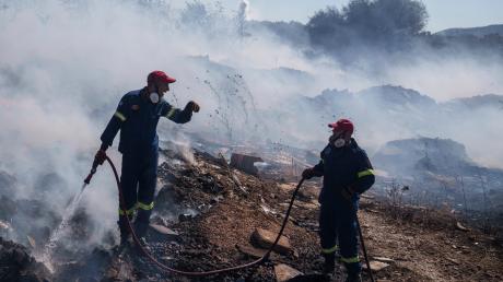 Feuerwehrleute versuchen, ein Feuer zu löschen, während ein Löschhubschrauber Wasser im Vorort Koropi im Osten von Athen abwirft.