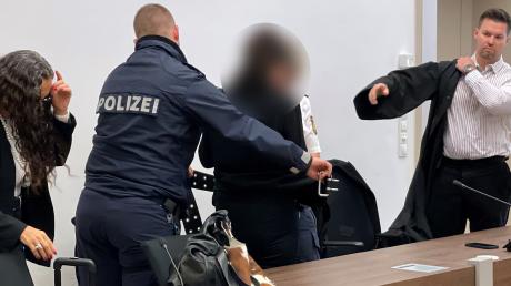Ein Polizist nimmt der Angeklagten die Bauchfesseln ab, bevor sie sich auf die Anklagebank im Landgericht Memmingen setzt.